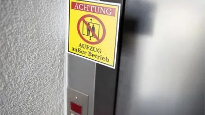 An einer Aufzugtür hängt ein gelbes Schild mit roter Aufschrift, dass der Aufzug außer Betrieb ist.