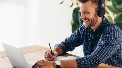 Mann mit Headset sitzt lächelnd vor einem Laptop