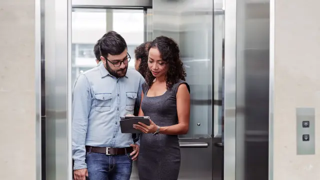 man and woman looking at a phone while standing in an elevator