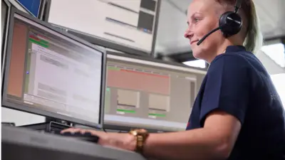An employee in the Bosch Monitoring Center looks at her screens; she is wearing a headset and has her hands on the keyboard in front of her.