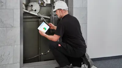 El montador esta de rodillas con una tablet delante del ascensor y utiliza Bosch Elevator Cloud para analizar los datos del ascensor.
