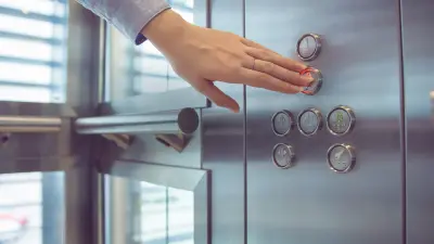 Hand drückt Knopf in einem Aufzug