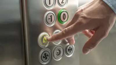 Eine Hand drückt den Notrufknopf in einem Aufzug.